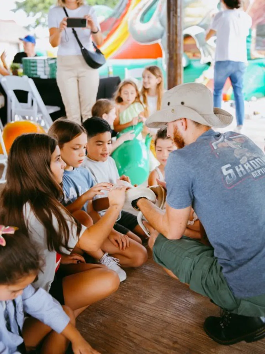 Circle of children reaching in to touch a snake at an outdoor community event