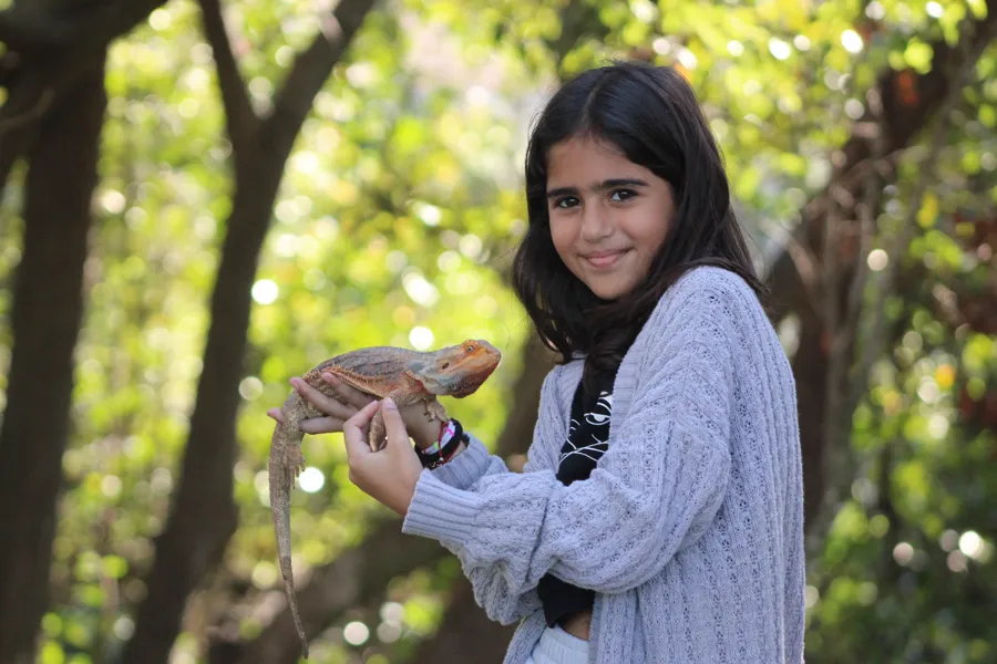 Girl posing with a bearded dragon among trees during a golden-hour photo session