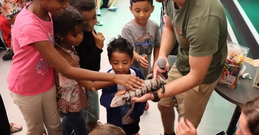 Handler with a microphone letting a crowd of kids pet a blue tongue skink at an indoor program